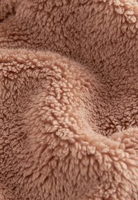 Tessuto in pile morbido, peloso, marrone chiaro con fibre ricce e strutturate che creano una superficie accogliente, calda e tattile.