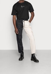 Musta puuvillainen T-paita valkoisella logolla, yhdistetty kaksivärisiin cargo-housuihin (musta ja kerma), sekä mustiin nilkkureihin. Sileä pinta, rento istuvuus.