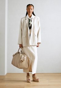 Béžový blazer a sukně, krémový vzorovaný šátek, taupe kabelka a boty na platformě. Hladké textury, uvolněný střih, minimalistický design.