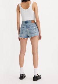 Vaaleansiniset farkkushortsit, joissa on purkautunut helma, kaksi takataskua ja logopatchi. Yhdistettynä valkoiseen tank toppiin ja mustiin kenkiin.