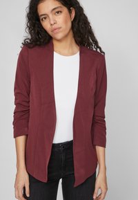 Bordowa marynarka z kołnierzem szalowym, długimi rękawami i otwartym frontem. Gładka faktura, w zestawieniu z białym topem i ciemnymi dżinsami.