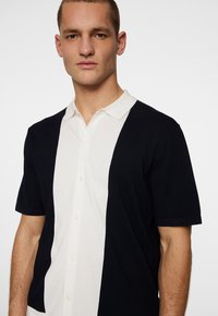 Koszulka polo z krótkim rękawem w kolorowe bloki; posiada sekcje w granatowym i białym kolorze, miękką tkaninę oraz klasyczny kołnierzyk z zapięciem na guziki.