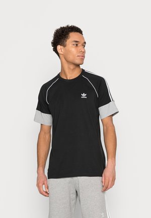 Svart bomull T-skjorte med grå oppbrettede ermer, hvite aksentstriper langs skuldrene, og en liten hvit Adidas-logo på brystet.