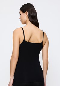 Canotta nera aderente con spalline sottili e regolabili, realizzata in materiale liscio, caratterizzata da un classico scollo tondo e un design semplice.
