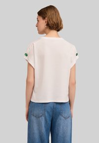 Vit kortärmad skjorta med avslappnad passform, med gröna detaljer vid ärmarna. Matchad med vida blå denimjeans.