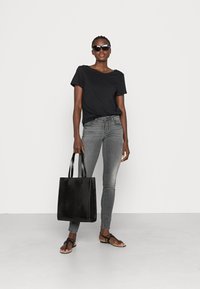 Zwarte t-shirt, grijze slim fit jeans, zwarte handtas met krokodillenprint en zwarte teenslippers; model draagt oversized zwarte zonnebril.