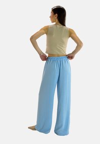 Lichtblauwe, wijde broek van zachte stof met een elastische tailleband. Gepresenteerd op een model met de rug naar de camera, gecombineerd met een beige top.