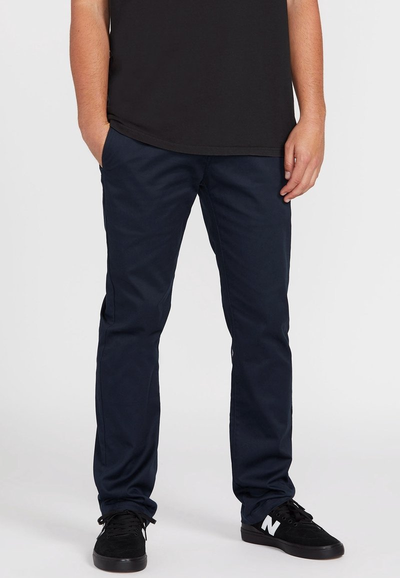 Marineblaue Baumwollhose mit geradem Bein. Verfügt über Vorderseiten-Taschen und eine glatte Textur. Getragen mit schwarzen Sneakern.