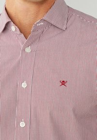 Chemise à rayures rouges et blanches en coton, avec un col boutonné et un petit logo rouge brodé sur la poitrine.
