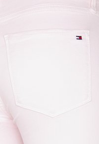 Jeans de denim rosa claro con un bolsillo tipo parche que lleva un pequeño logo bordado compuesto por franjas rojas, blancas y azules.