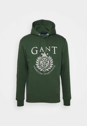 Grön hoodie gjord av mjukt tyg, med en vit logotyp och emblemdesign på framsidan, justerbar dragsko och ribbade muddar samt fåll.