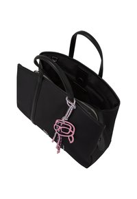 Svart tote-bag laget av syntetisk materiale med dobbelthåndtak, glidelås, og en rosa tegneserieaktig vedheng festet. Innvendig har den et rom.