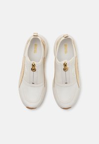 Hvite og beige slip-on sneakers med teksturdesign, gullglidelåsdetalj og gummisåle. Har en glatt syntetisk overdel.