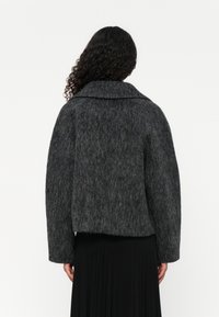 Giacca di lana grigia chunky con ampio colletto, spalle cadute e vestibilità oversized. Superficie texturizzata e dettaglio dell'orlo dritto sul retro.