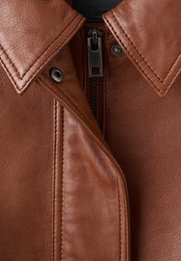 Brązowa skórzana kurtka z尖ym kołnierzem, zamkiem błyskawicznym i kontrastującymi szwami wzdłuż krawędzi klapki oraz ciała kurtki.