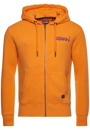 Lyse orange hættejakke med lynlås, snøretrækshætte, forlommer og lilla "Superdry" logo på brystet samt et lille mærke nær lommen.