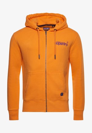 Sweat à capuche zippé orange vif avec cordon à la capuche, poches avant, logo violet "Superdry" sur la poitrine et petite écusson près de la poche.