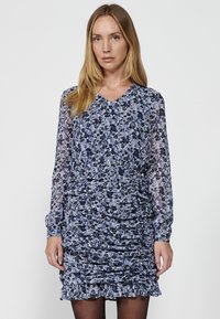 Kukallinen mini mekko sinisen ja violetin sävyissä, jossa on pitkät läpikuultavat hihat, V-mallinen kaula-aukko ja kerätyt yksityiskohdat vartalon alueella.