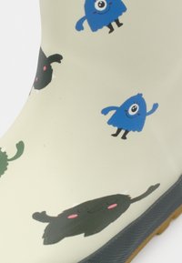 Botte en caoutchouc blanc cassé avec des monstres de dessin animés colorés : créatures souriantes à un œil bleues et formes noires et vertes souriantes avec des joues roses.