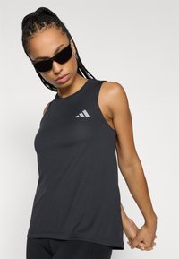 Μαύρο αθλητικό τοπ χωρίς μανίκια με στρογγυλή λαιμόκοψη, κατασκευασμένο από μαλακό, ελαστικό ύφασμα. Διαθέτει ανακλαστικό λογότυπο Adidas στο αριστερό μέρος του στήθους.