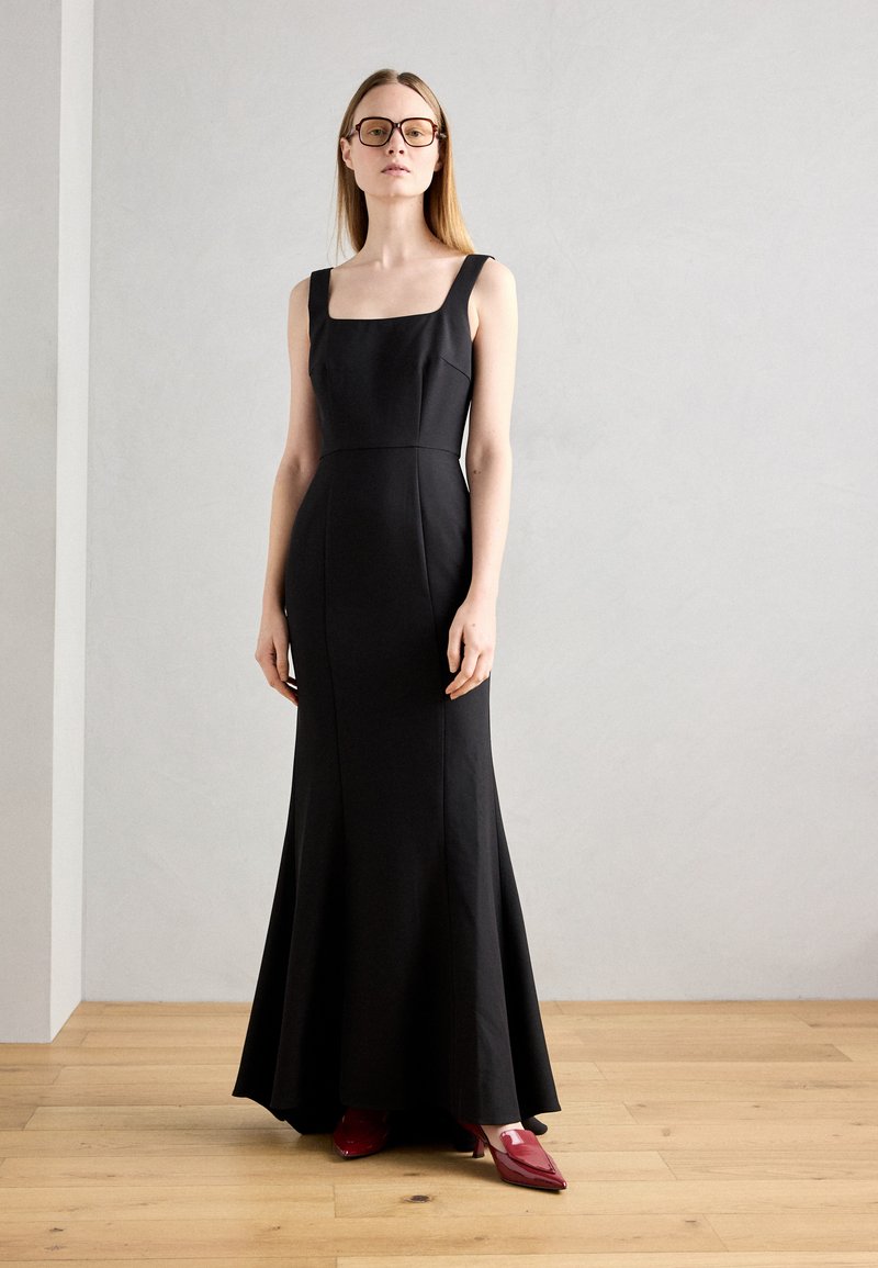 Black sleeveless gown with a square neckline, fitted bodice, flared skirt, and red glossy heels. Smooth fabric with minimal seams.