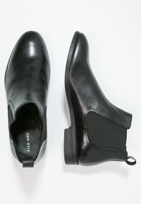 Botas de tobillo de cuero negro con paneles elásticos en los laterales, punta redondeada y pequeño tacón negro. Textura suave con una tira en la parte trasera.