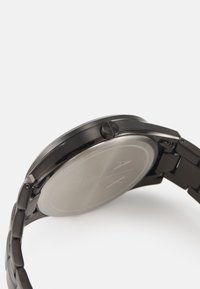 Orologio in acciaio inossidabile nero con cassa rotonda, bracciale in metallo e retro liscio di tonalità argento con dettagli del logo incisi.