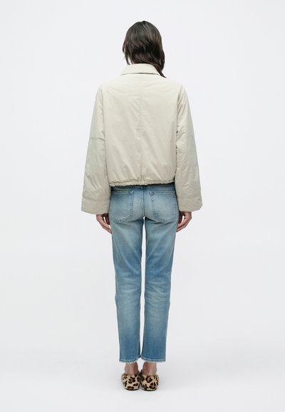 Μπεζ κοντή ζακέτα με φαρδιά μανίκια, συνδυασμένη με ανοιχτό μπλε τζιν παντελόνι κανονικής γραμμής και παντόφλες με λεοπάρ σχέδιο. Μινιμαλιστικός σχεδιασμός και υφές.