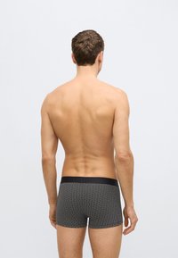 Fekete trunk stílusú alsónemű texturált mintával, egyszínű fekete derékpánttal. Az anyag elasztikusnak és testhezállónak tűnik.