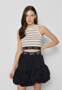 Czarna spódnica z falbaniastymi warstwami i pasem z logo "BIZUU"; w połączeniu z beżową, prążkowaną crop top, o dopasowanym fasonie.