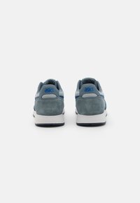 Ténis desportivos azuis em pele camurça com parte superior em malha, entressola branca e sola em borracha preta; apresenta um logótipo ASICS proeminente em azul.