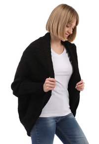 Cárdigan negro de punto con un patrón de rombos texturizado, de frente abierto y con mangas acanaladas, llevado sobre una camiseta blanca y jeans azul.