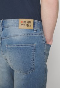 Šviesiai mėlynos džinsinės kelnės su etiketėmis "DENIM PROJECT" nugaros juosmens dalyje, turinčios klasikinį penkių kišenių dizainą ir siuvinėjimo detales.