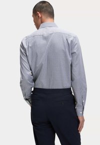 Camicia a quadri blu e bianca con colletto allargato, maniche lunghe e polsini a contrasto, abbinata a pantaloni blu scuro.