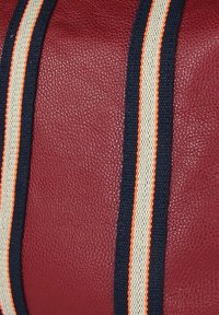 Rode, gestructureerde leren oppervlakte met twee parallelle stoffen riemen in marineblauw, wit en dunne oranje strepen.