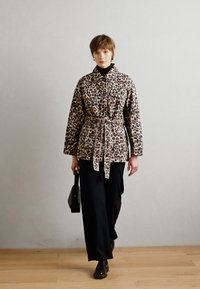 Veste imprimée léopard avec une taille ceinturée, des manches longues, un col et deux poches avant, associée à un pantalon noir à jambes larges et des bottines.