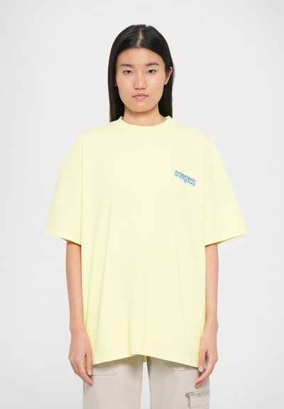 Gul oversized t-shirt lavet af bomuld, med korte ærmer, en rund halsudskæring og et blåt logo på venstre brystområde.