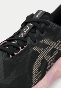 Zwarte sportieve schoen met een gestructureerde bovenkant, voorzien van roze accenten en een opvallend logo. Inclusief zwarte veters en een gevoerde zool.