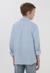 Camicia a righe blu chiaro con maniche arrotolate, design con colletto e vestibilità rilassata. Il tessuto appare morbido, adatto per un abbigliamento informale.
