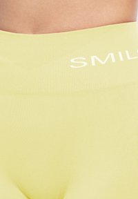 Jasnożółte legginsy z wysokim stanem o rypsowanej teksturze i białym napisem "SMILE" na pasku, zapewniające dopasowane wydanie.