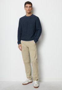 Marineblauer Strickpullover, beige Hose und weiße Sneaker mit Kautschuksohlen. Der Pullover hat einen Rundhalsausschnitt und gerippte Bündchen für Details.