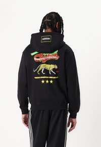 Sweatshirt preto com capuz, apresentando uma estampa gráfica colorida com uma onça, texto "Originals" e três estrelas. Feito de um material suave em mistura de algodão.