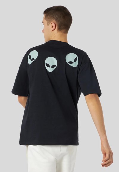 T-shirt in cotone nero con tre stampe di teste aliene azzurre sul retro. Maniche corte, vestibilità morbida e design a collo rotondo.