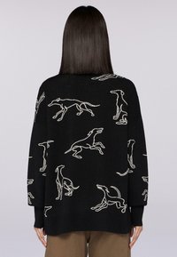 Schwarzer Pullover mit tanfarbenen Hundesilhouetten in verschiedenen Posen, oversize Passform, langen Ärmeln und weichem, strukturiertem Stoff.