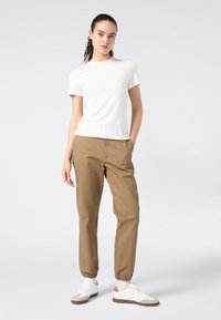 T-shirt bianco a maniche corte abbinato a chinos beige dal taglio rilassato e sneakers bianche con dettagli marroni. Tessuto morbido, design semplice e tasche.