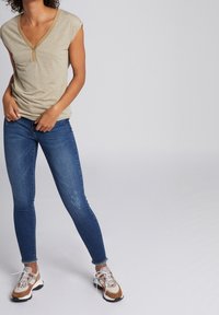 Beige kortärmad topp med V-ringning och brun kant, kombinerad med mörkblå smala jeans. Skorna har beige, bruna och grå detaljer.
