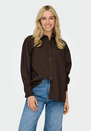 Brown long-sleeve shirt with a button-up design, relaxed fit, and a smooth texture; paired with light blue wide-leg jeans.