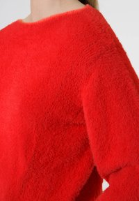 Pull rouge texturé au design carré avec un col large. Présente une finition douce et duveteuse ainsi qu'un détail de couture diagonale traversant le tissu.