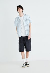 Majica s kratkimi rokavi, svetlo modri z navpičnimi črtami, nad belim majico, v kombinaciji s temnimi jeans kratkimi hlačami in črnimi supergami z belimi detajli.