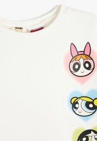 Sudadera blanca con tres caras de personajes de dibujos animados dentro de formas de corazón. Los personajes están contorneados con líneas negras gruesas y acentos de color.